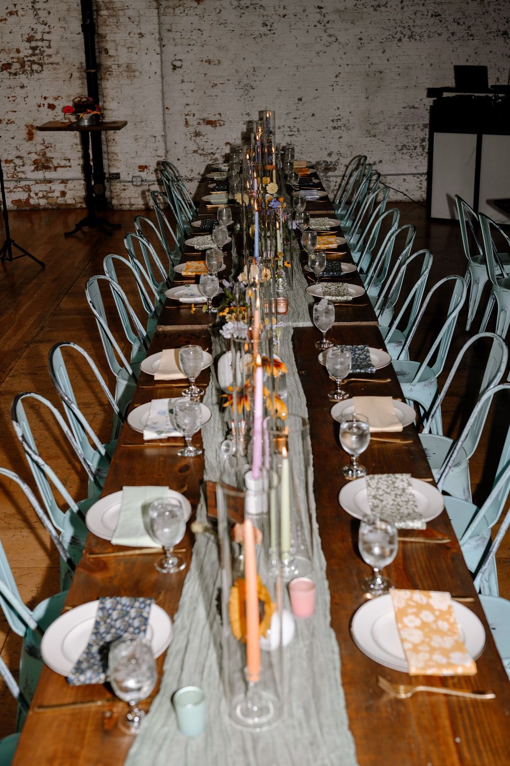 Elegant table settings with wine glasses and blue chairs line long wooden tables in an industrial wedding venue.