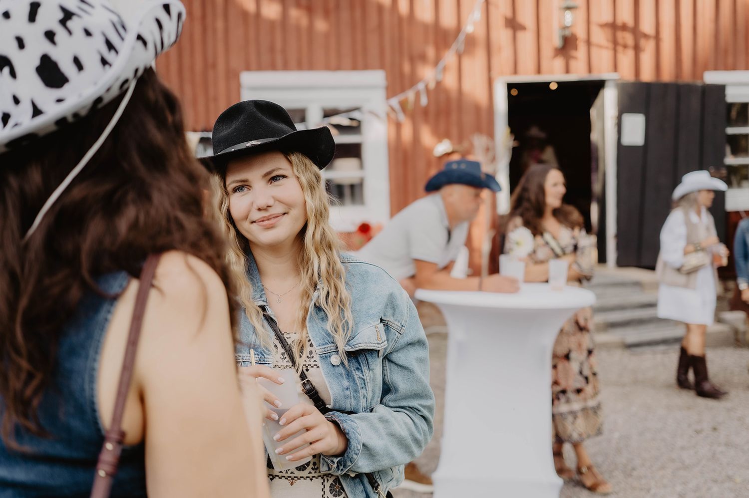 Gäster i snygg western outfits under mingel i kvällssolen på en cowboyfest i Östergötland, foto av Lets Bloom Media.