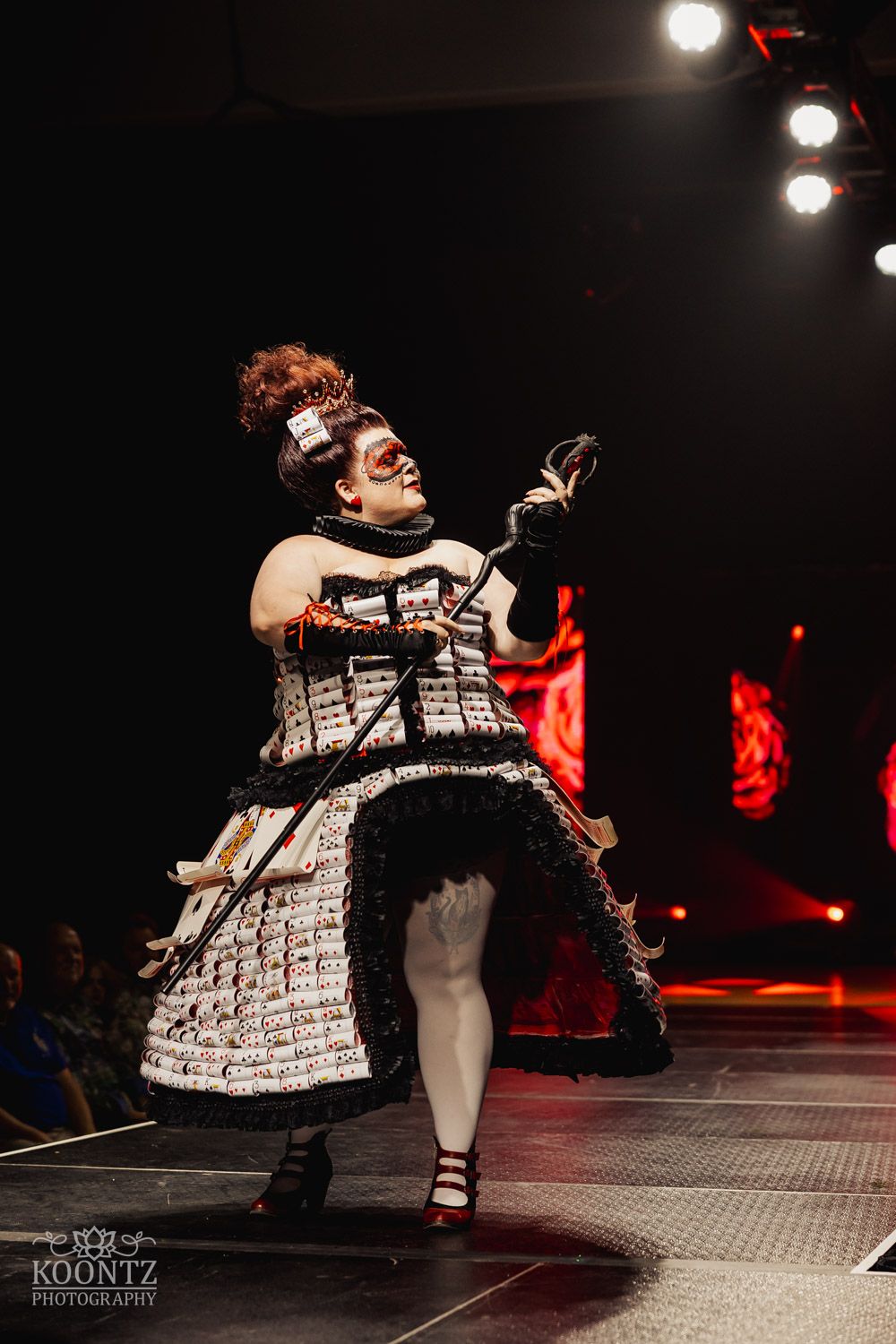 Performer in black and white newspaper print dress spins dramatically on dark stage during theatrical performance.