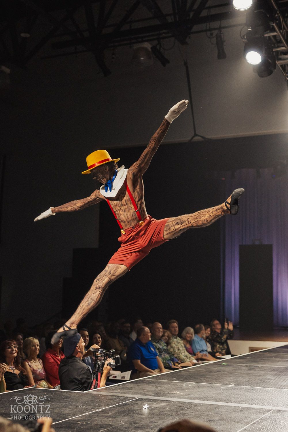 Dynamic breakdance performer executing an aerial move in an orange outfit on stage.
