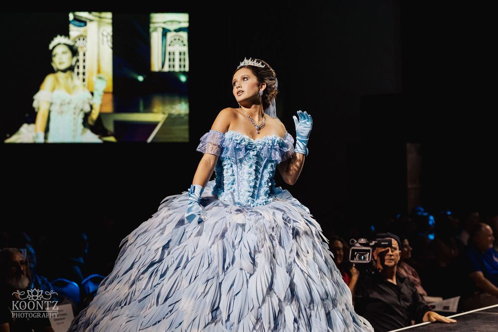Fashion model wearing an elegant white ballgown with dramatic ruffled skirt performs on a dark runway.
