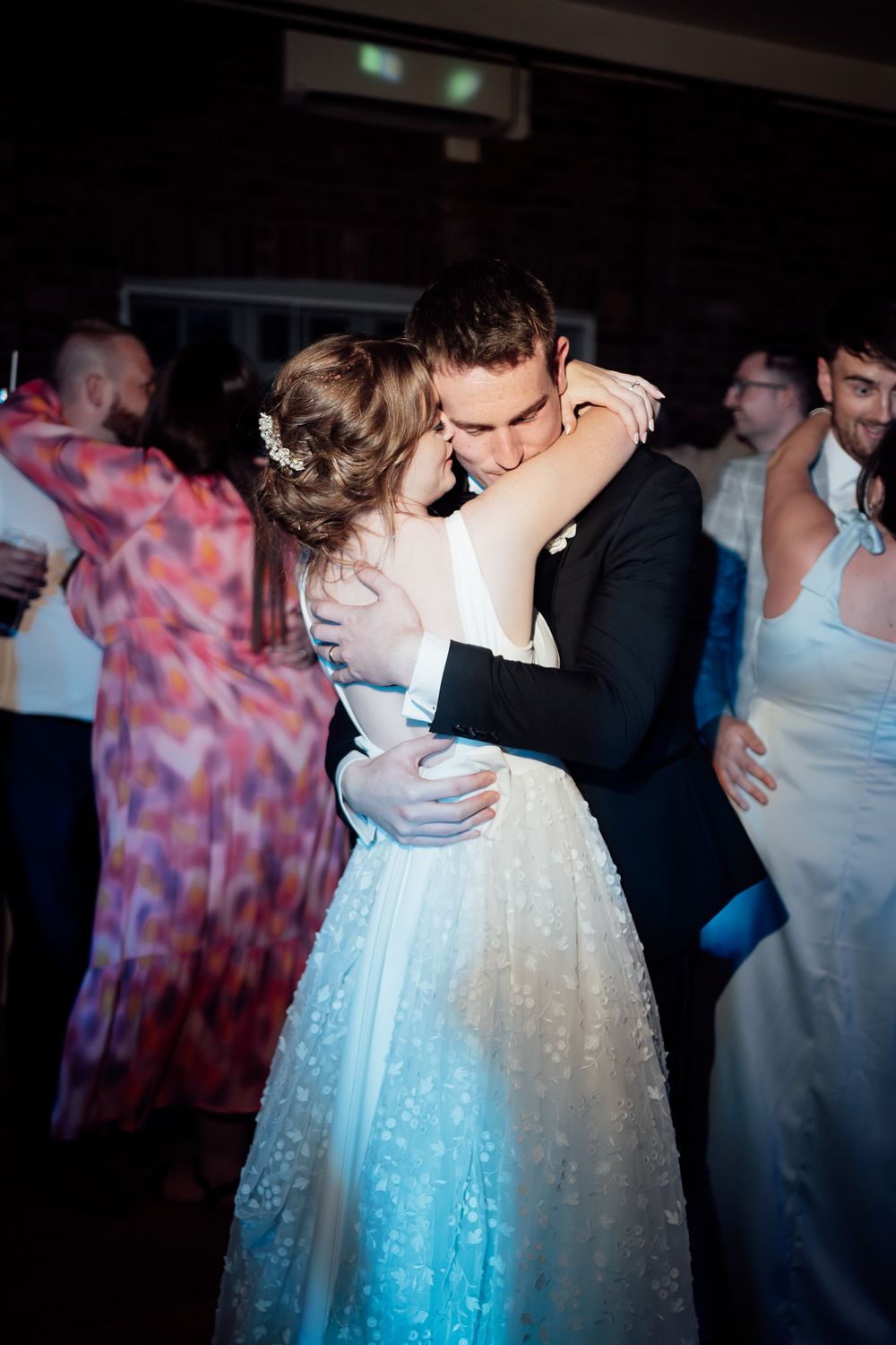A couple shares an intimate dance together during their wedding reception, with romantic lighting in the background.
