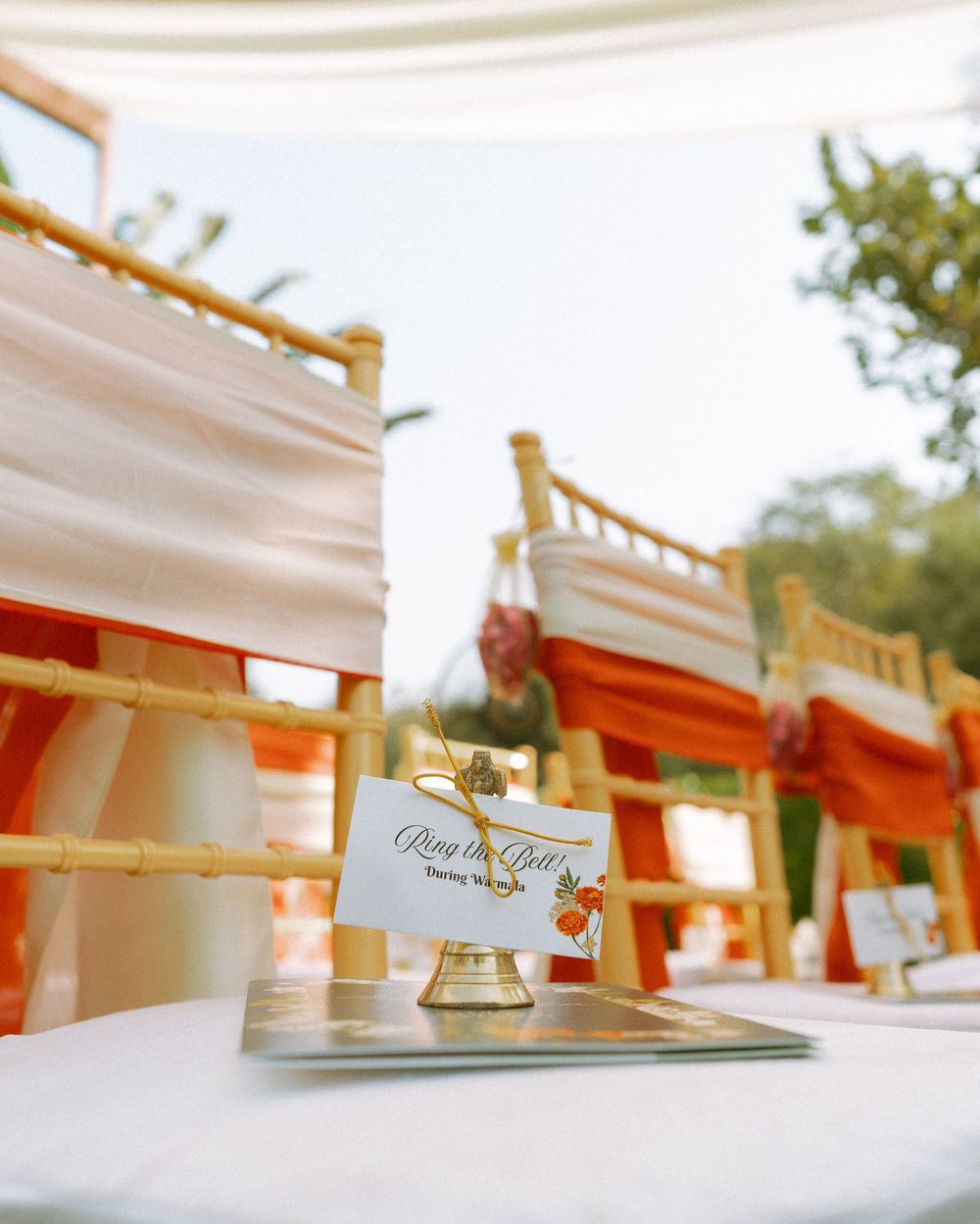 Wedding reception table settings with white linens and place cards in natural outdoor lighting.