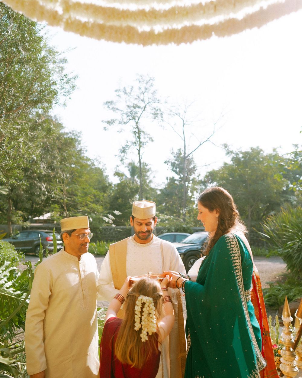 People in formal ethnic wear stand together under decorative floral arrangements at an outdoor venue.