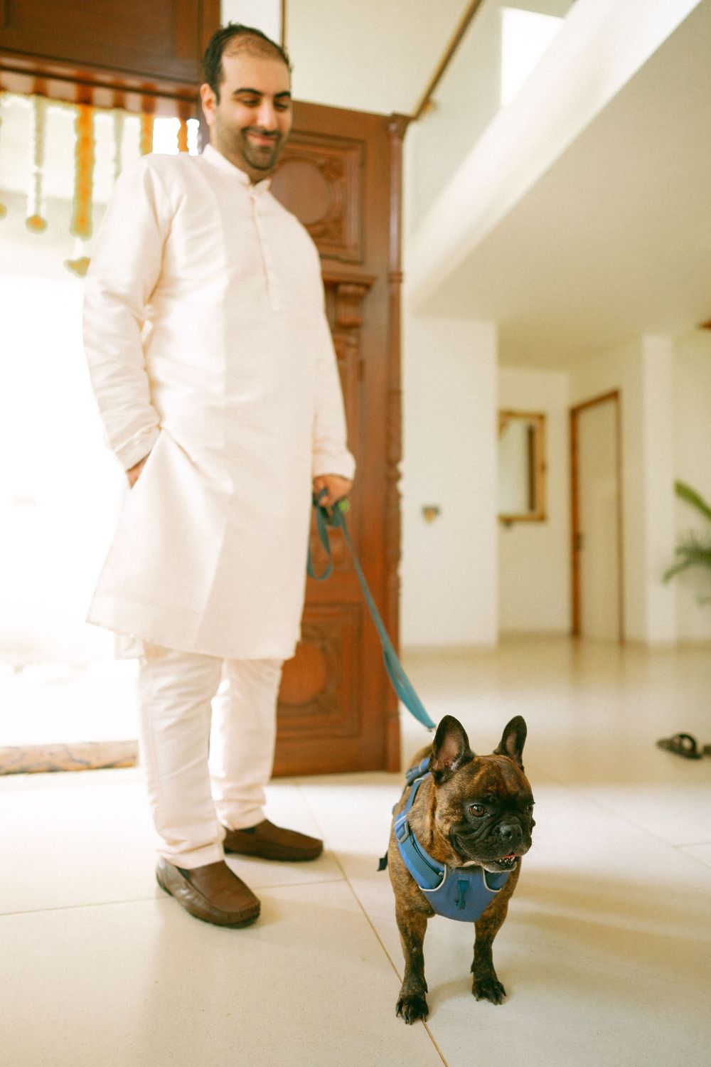 Person in white clothing walking alongside a small black dog in a bright indoor hallway.
