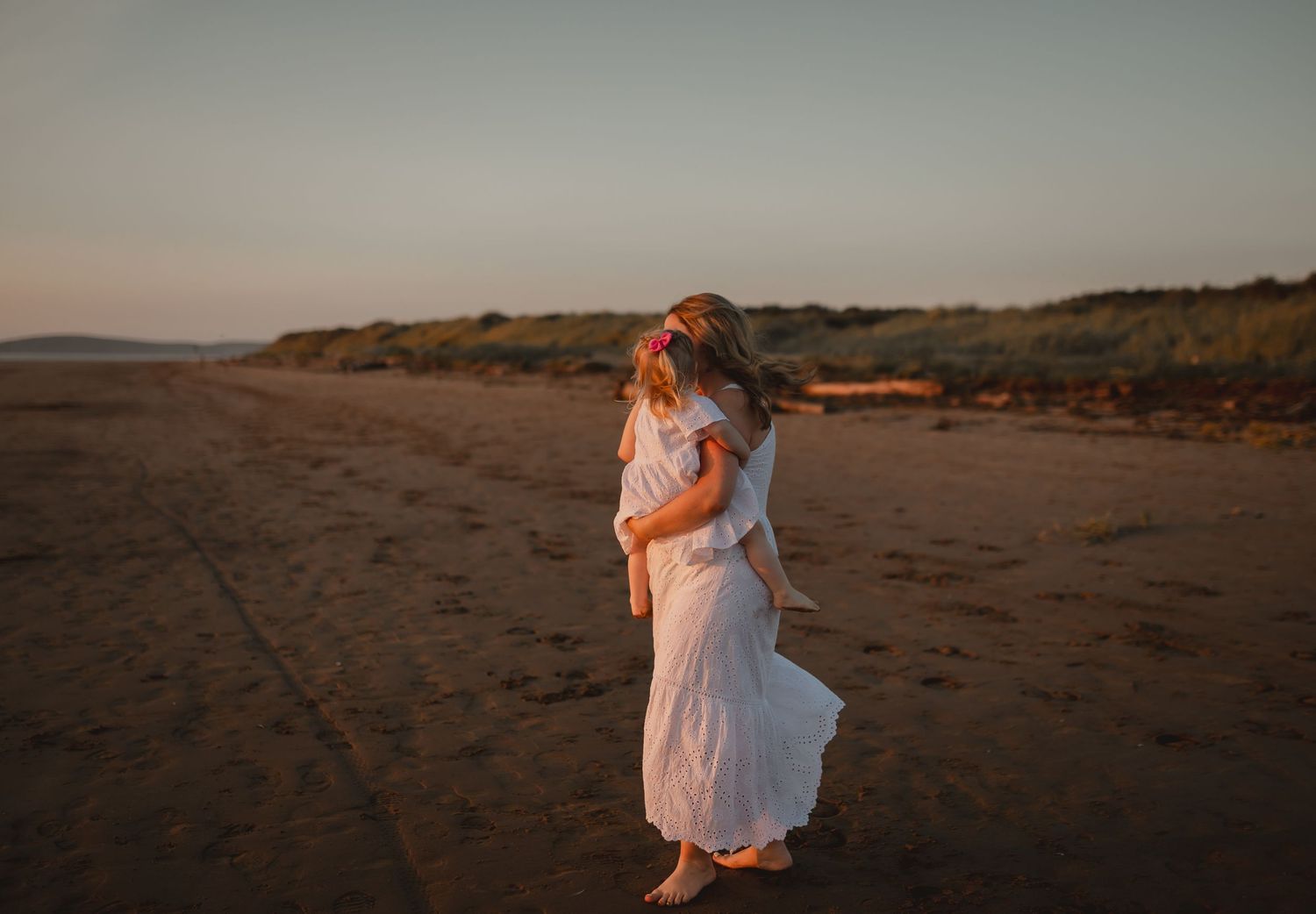 A mum spins her daughter around on a beach at sunset