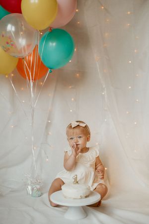 A series of four photos showing a cake smash photo session with colorful balloons and twinkle lights in the background.