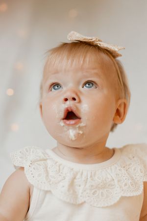 Baby wearing white lace dress with powdered sugar on face gazes upward with wide-eyed wonder.