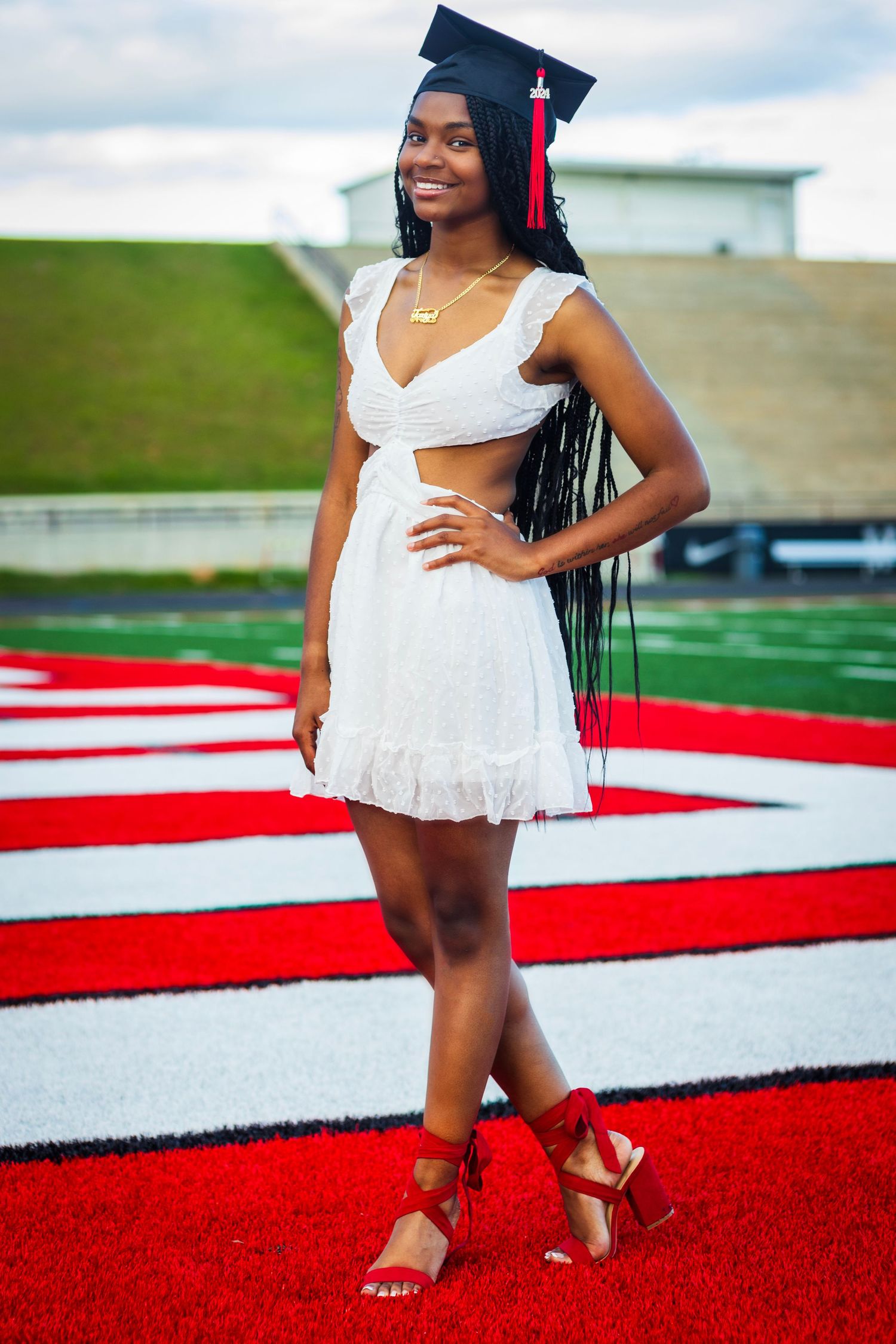 Graduate in white dress poses on red and white striped field.