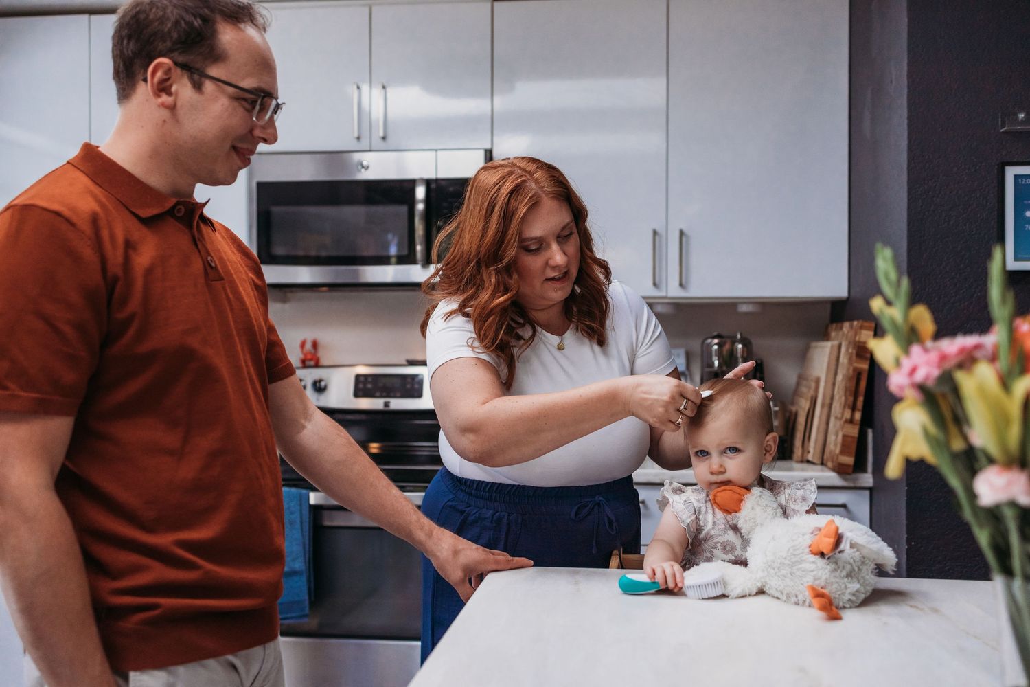 Family cooking together in modern white kitchen with baby sitting on counter and watching meal preparation.