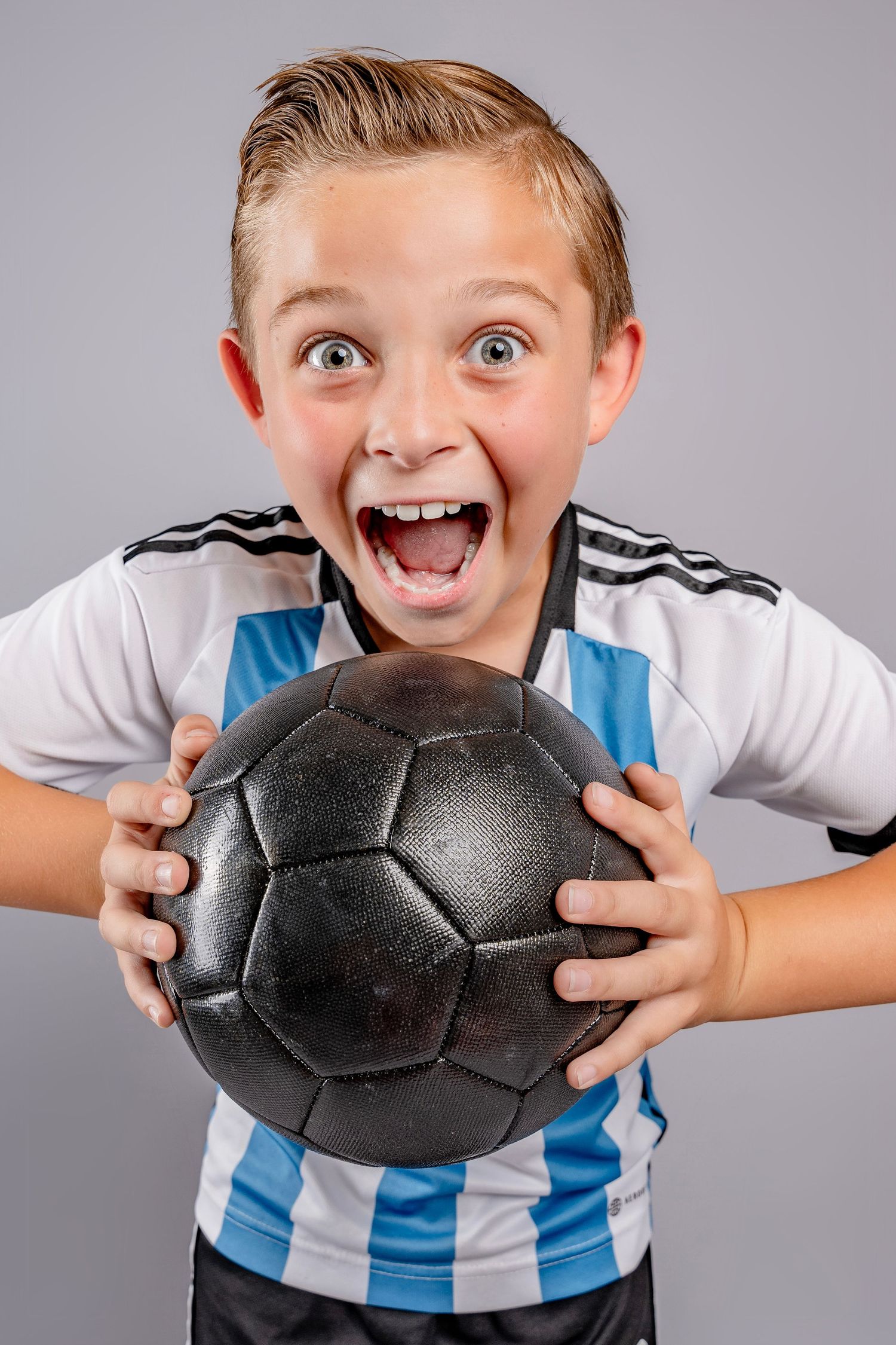 Sequence of an excited young fan in a blue and white striped jersey reacting playfully with a black soccer ball.