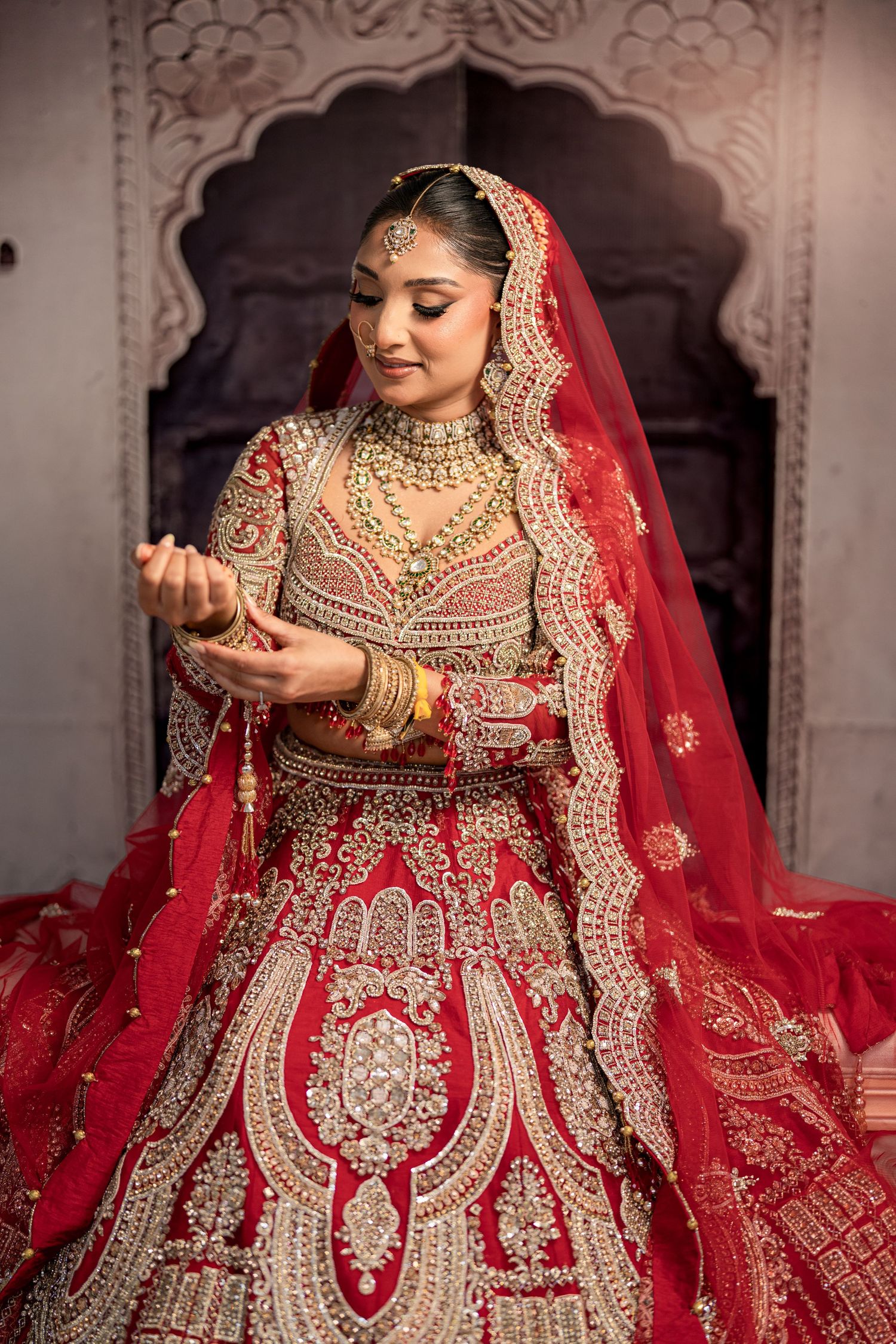 Traditional wedding couple in red lehenga and white sherwani pose on wooden bridge.