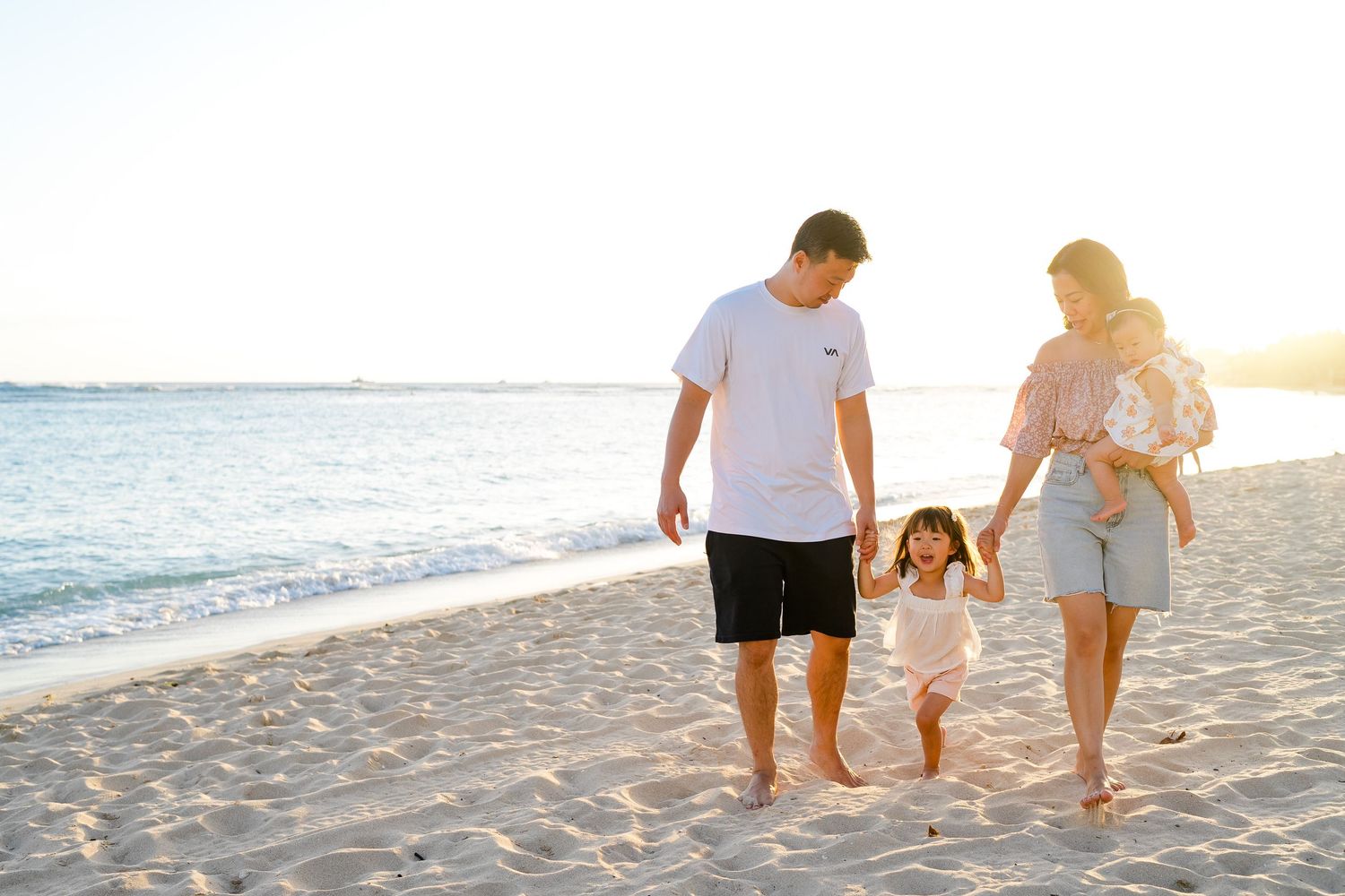 A person walks with their dog along a beach at sunset while holding a camera and photographing. Oahu family photography, Hawaii family photo