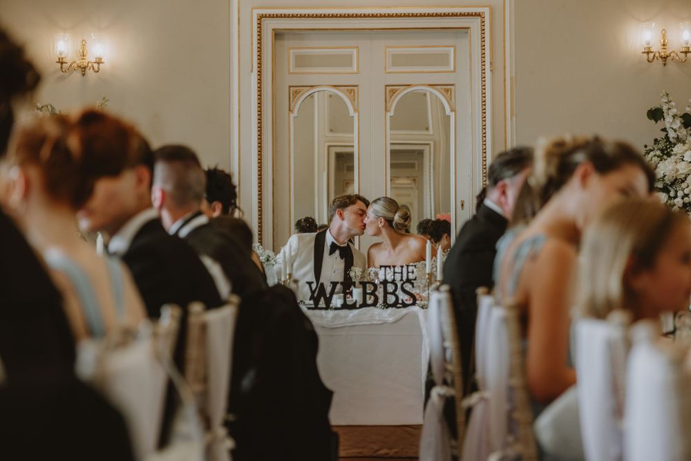 Wedding reception guests gather in an elegant room with chandelier and ornate white doors.