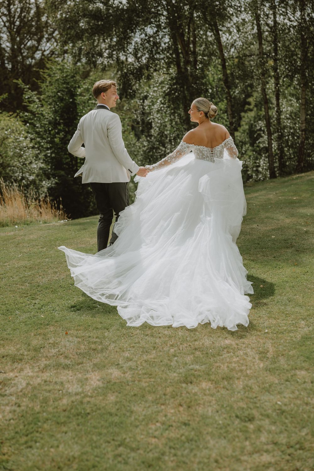 A romantic wedding photo of a couple walking through a wooded area, with the bride's flowing white dress trailing behind.
