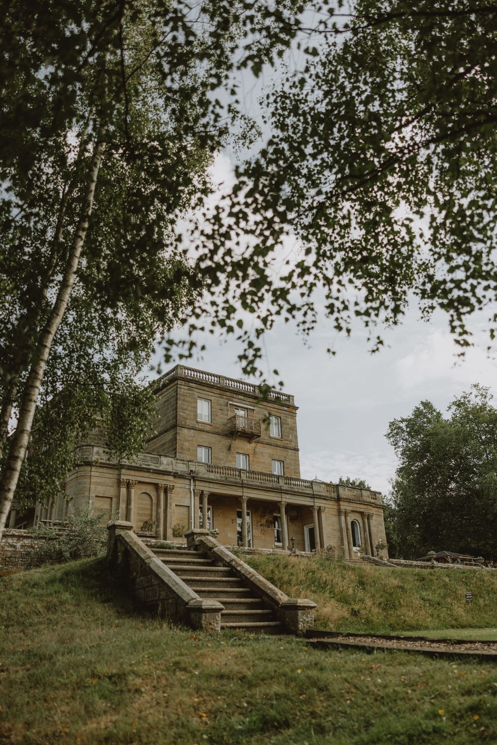 A grand historic mansion with stone steps and birch trees framing the architectural view.