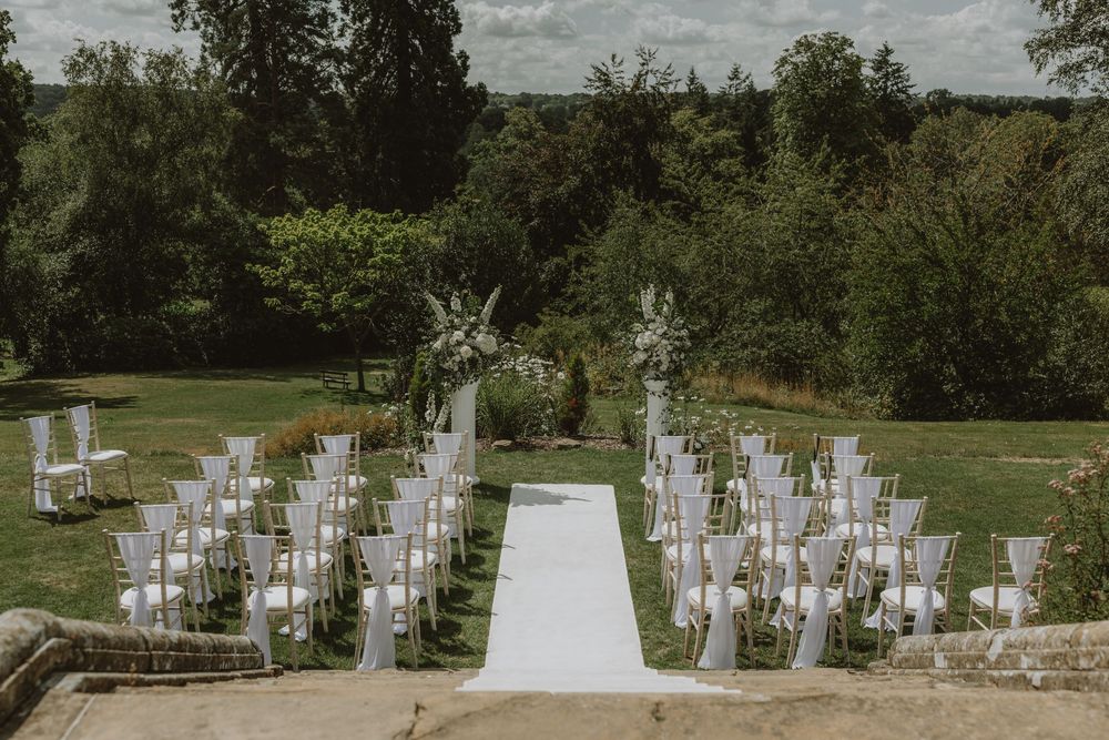 An outdoor wedding ceremony setup with white chairs and floral arrangements on a grassy lawn.