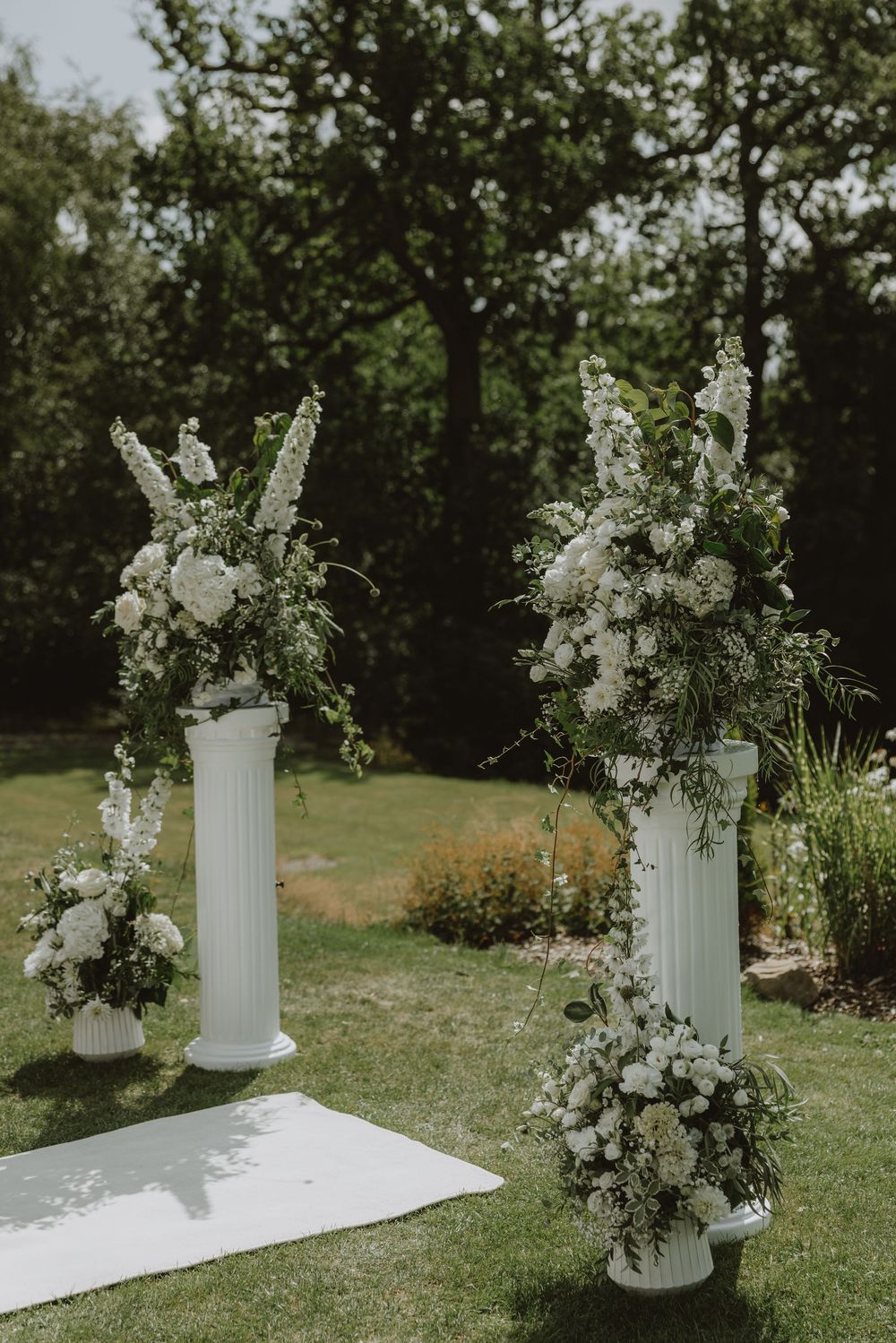 White floral arrangements on classical columns create an elegant outdoor wedding altar.