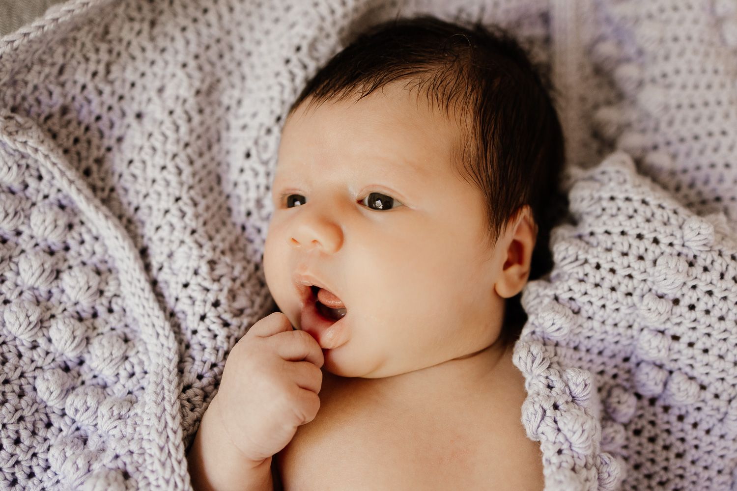 A baby looks curiously while wrapped in a knit blanket