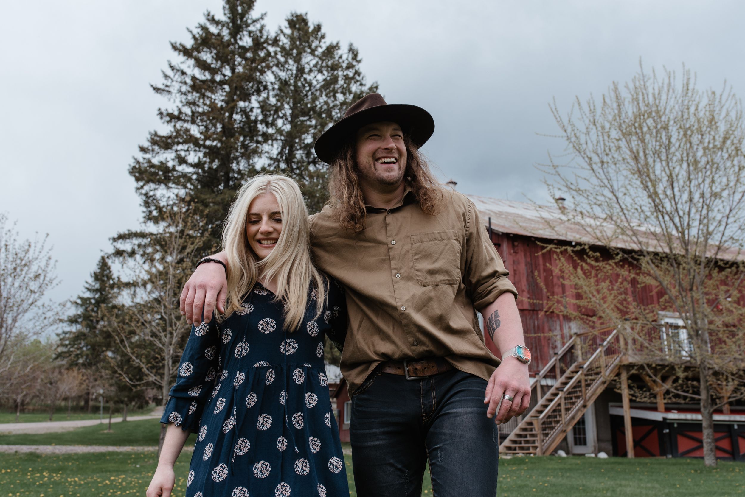 Two people walk together outdoors in casual clothing with a rustic red barn building in the background.