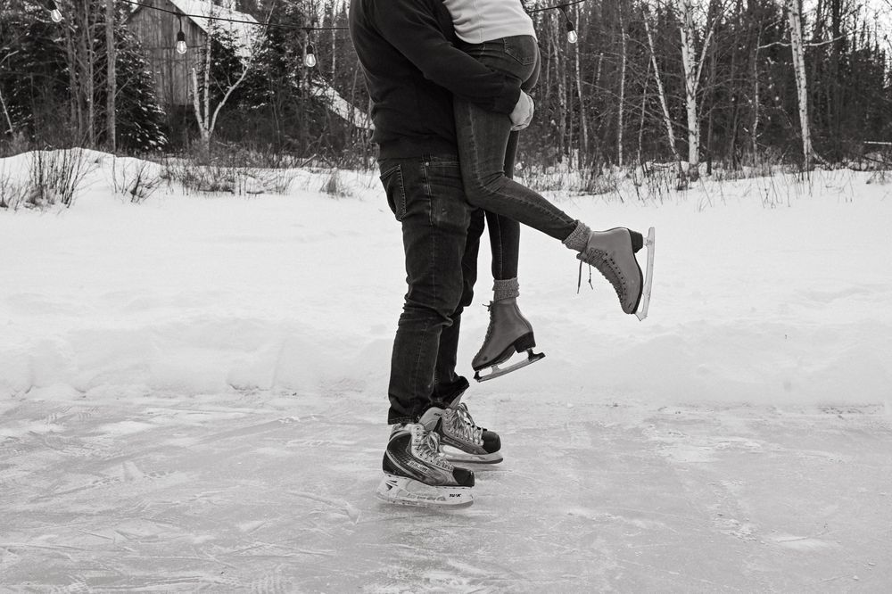People in ice skates gliding across a frozen lake in winter, surrounded by snow and trees.