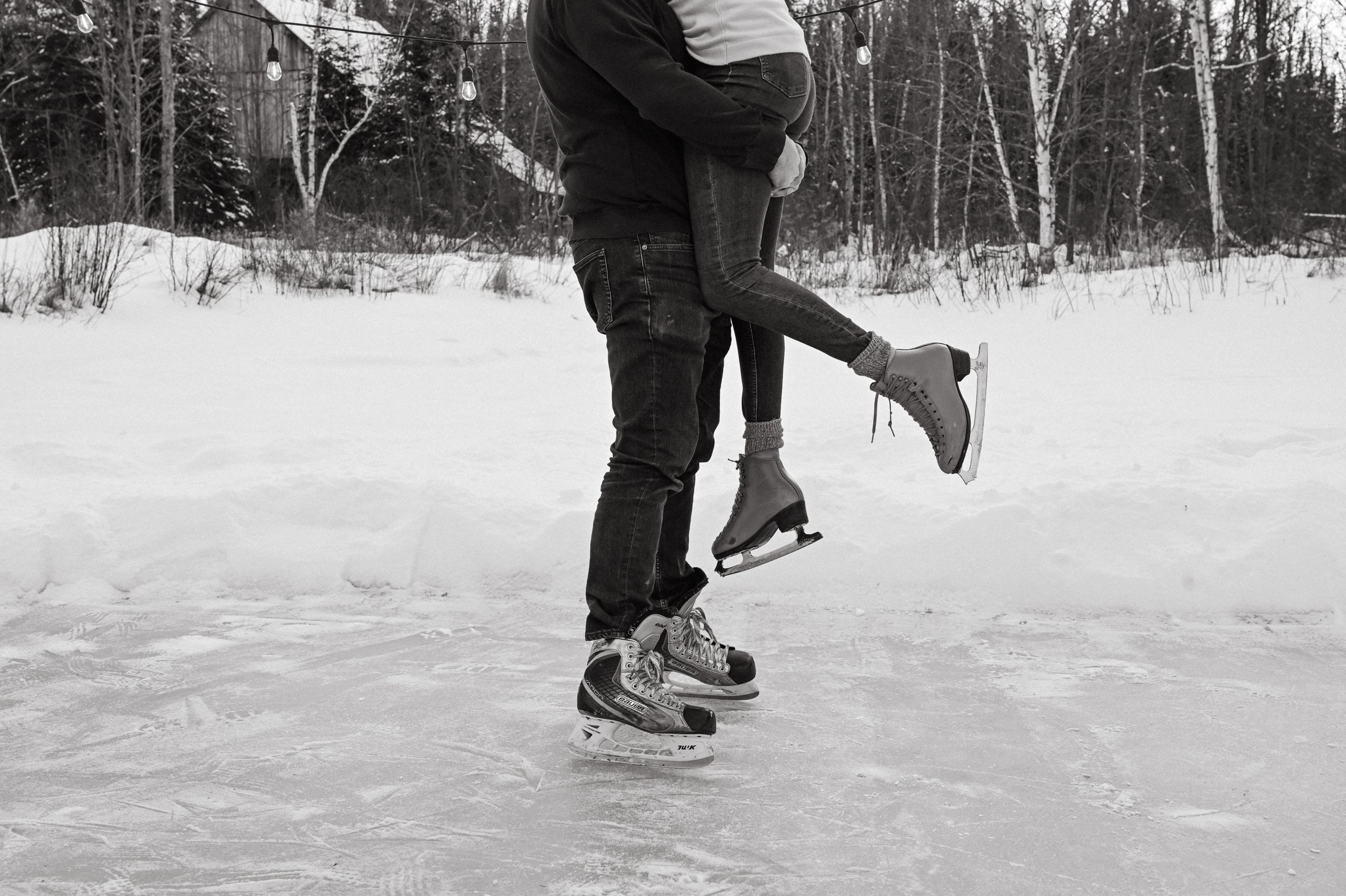 People in ice skates gliding across a frozen lake in winter, surrounded by snow and trees.