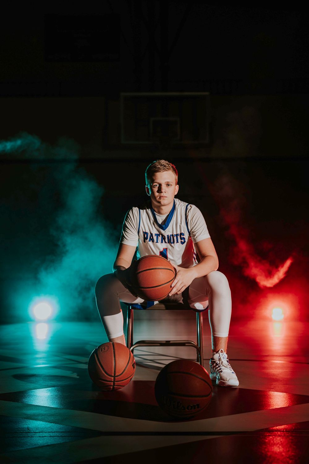 Basketball player in Patriots uniform sits on chair surrounded by dramatic lighting and smoke.