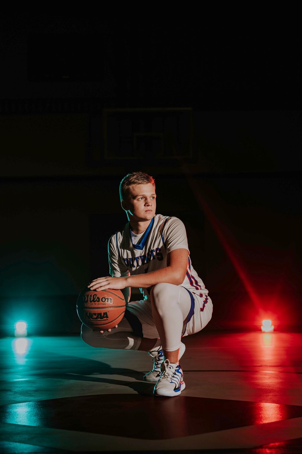 Basketball player poses with ball in dramatic lighting with red and blue smoke effects.