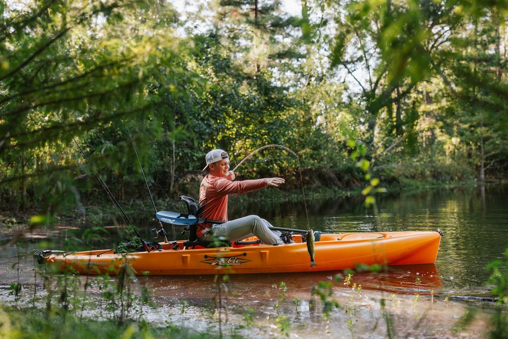 Orange kayak gliding across serene water with trees reflecting in the background.