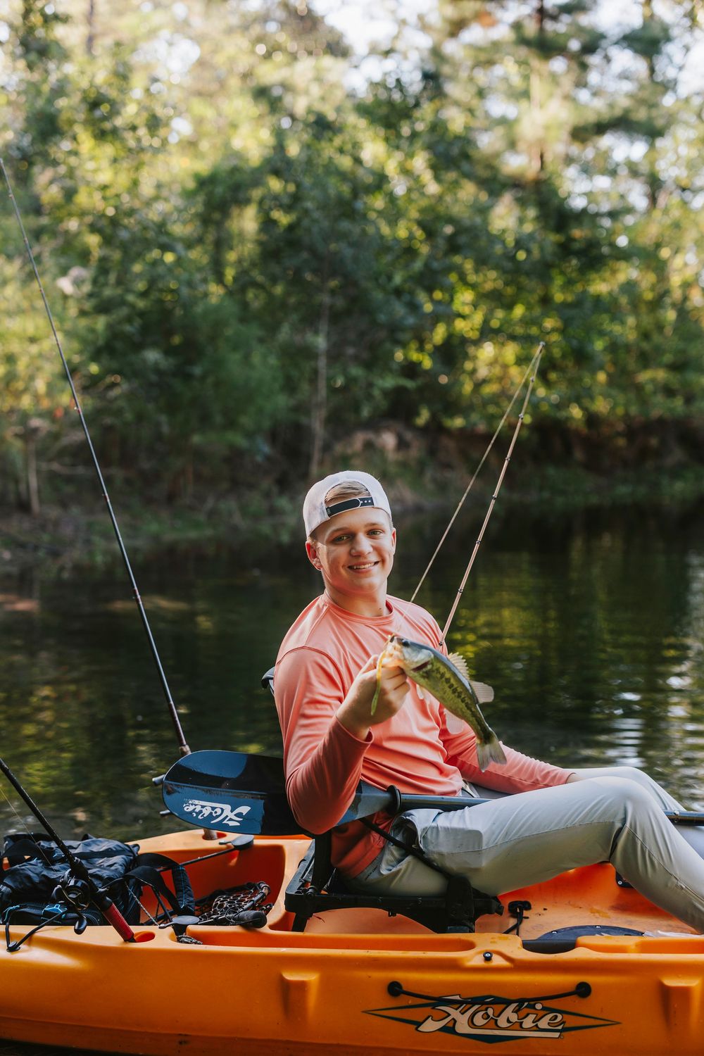 Person relaxing in an orange kayak on a peaceful lake surrounded by trees.