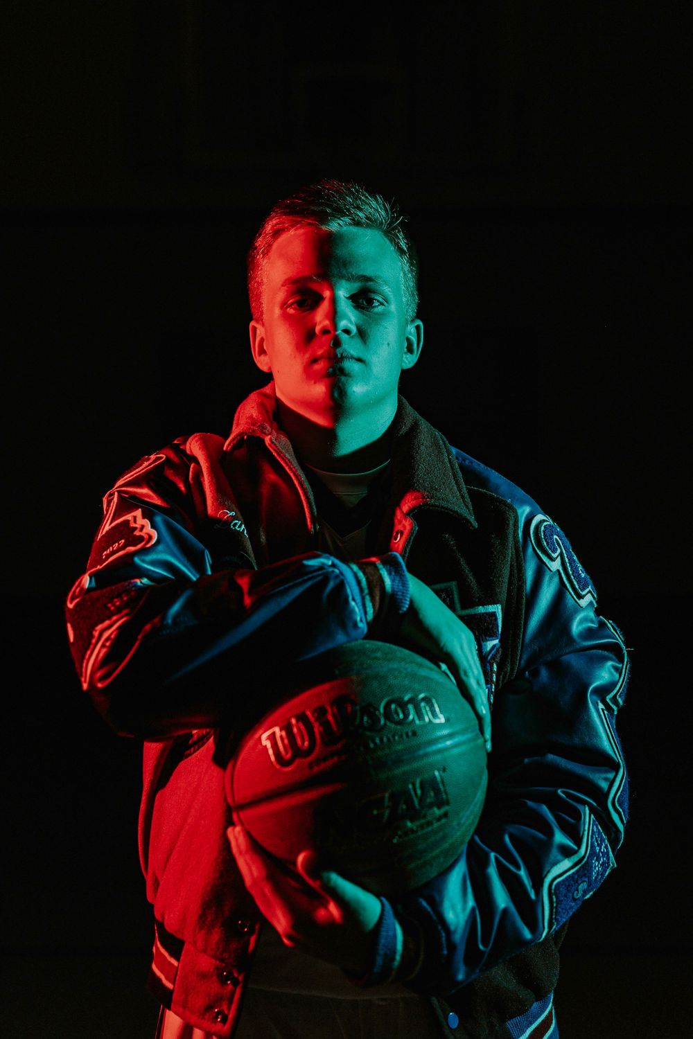 Dramatic portrait with red and blue lighting holding basketball.
