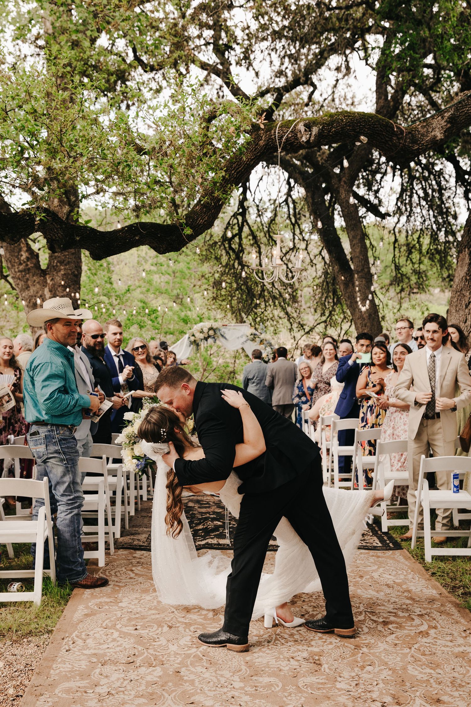 A couple in wedding attire embraces beside a rustic stone wall during their outdoor photo session.