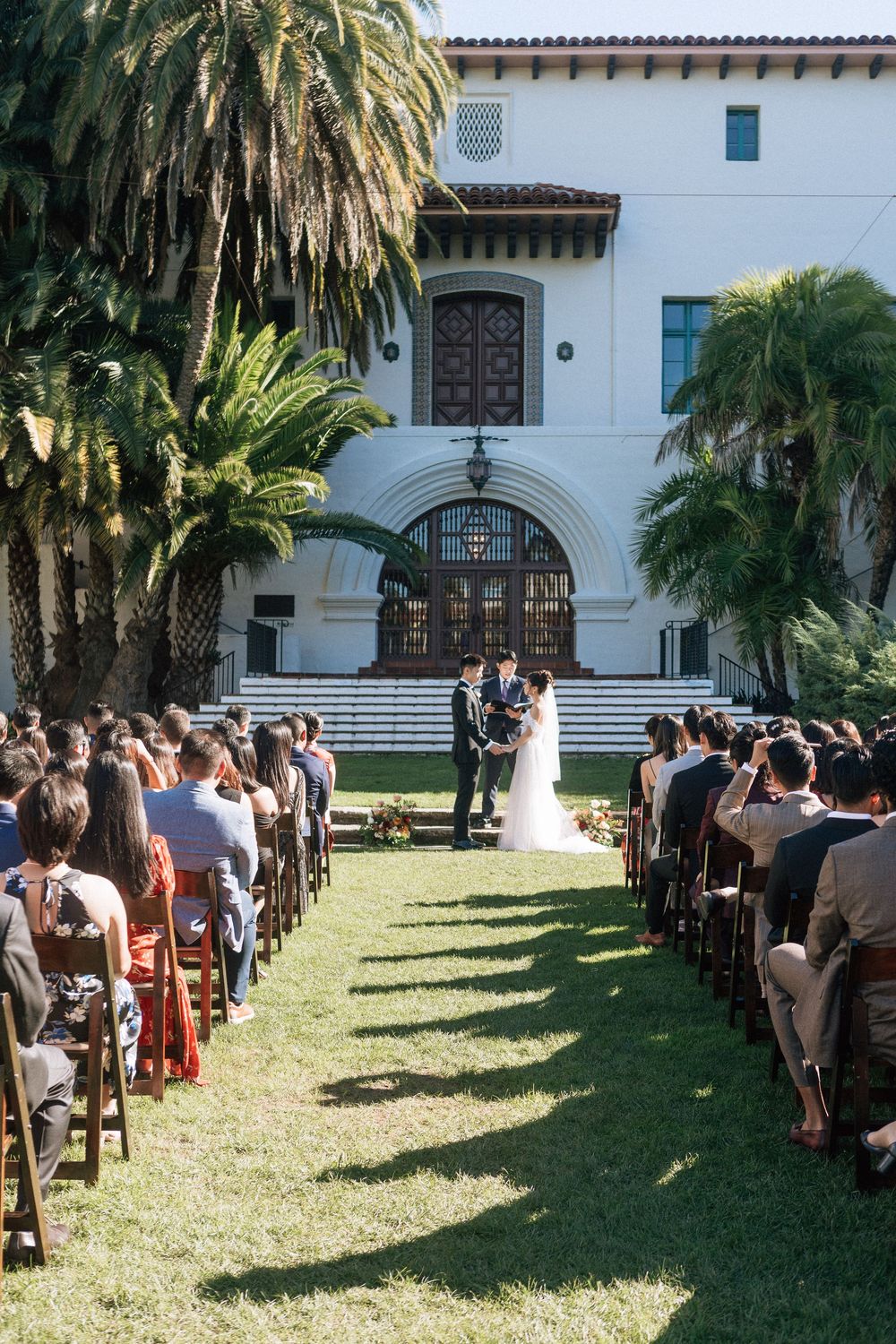 A wide shot of a wedding ceremony at the Sunken Gardens location at Santa Barbara Courthouse with wedding guests watching the ceremony.
