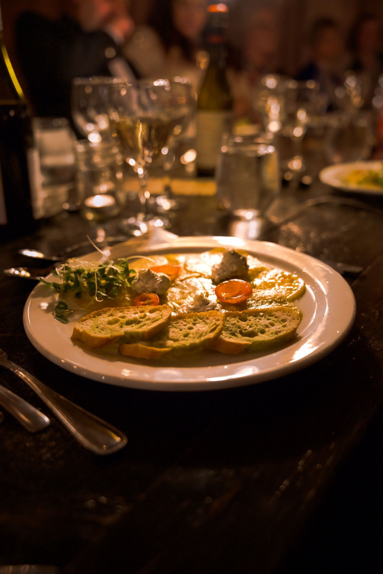 Elegantly plated appetizers served on white dishes at a dimly lit dinner.