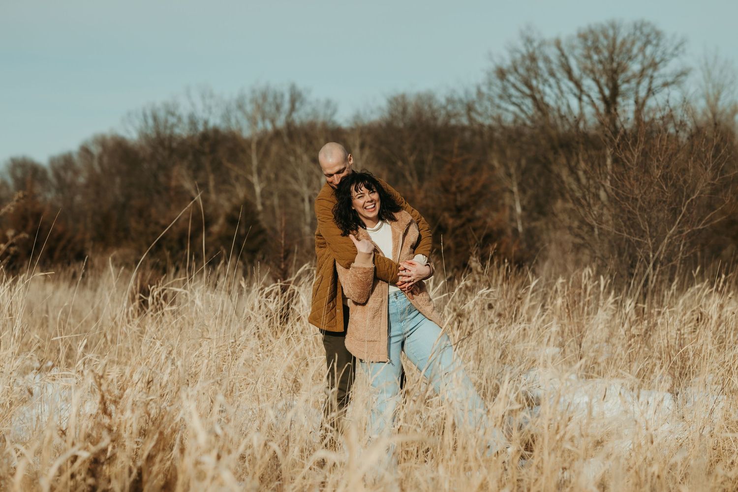 A couple walks together through an evergreen forest during golden hour sunset.