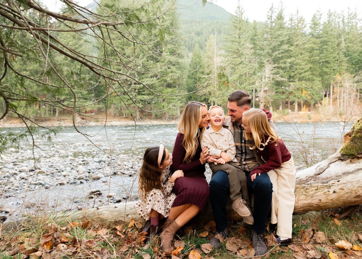 Family of three shares joyful moments together on a rocky riverbank surrounded by autumn trees.