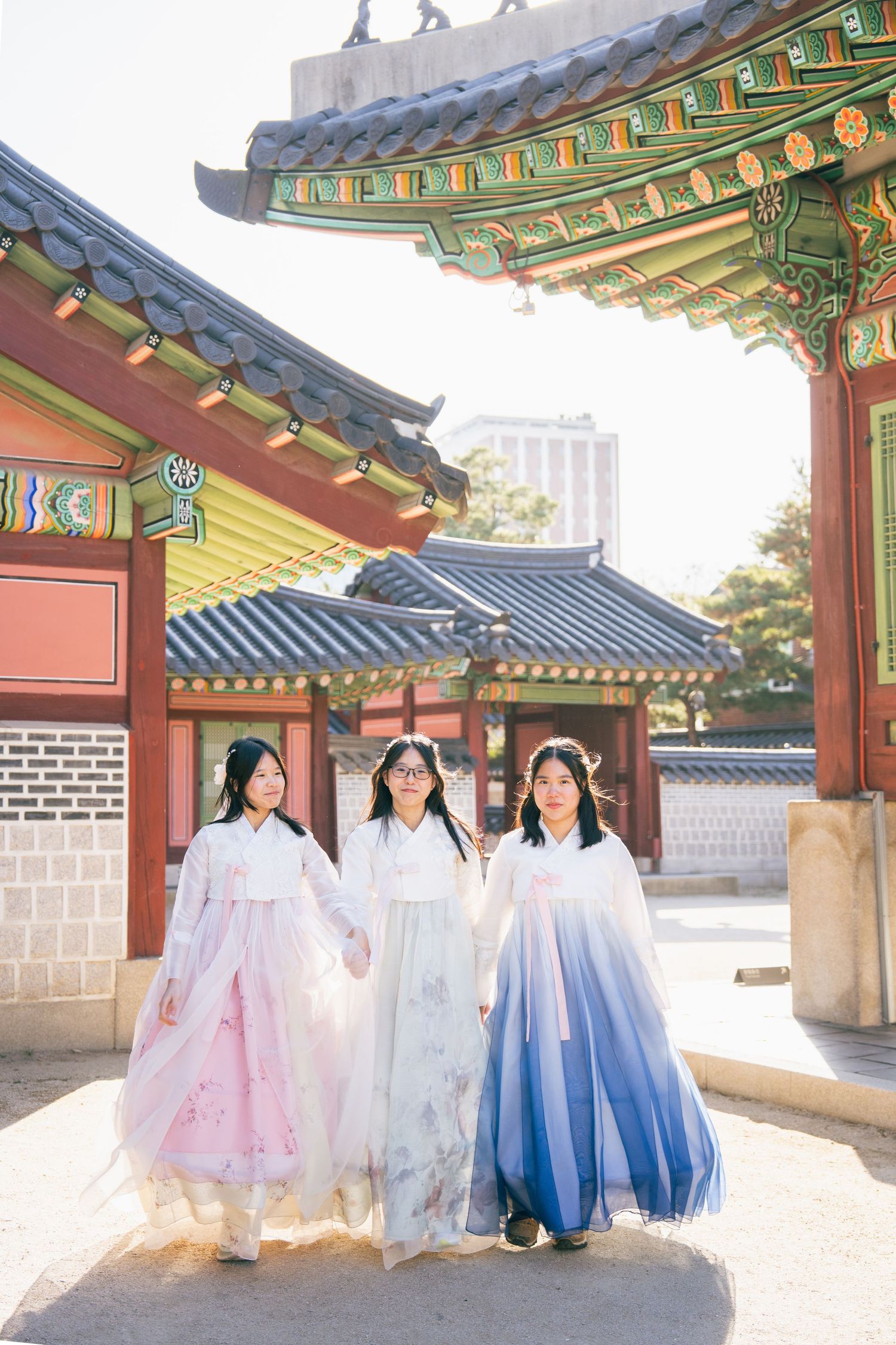 A group wearing traditional Korean hanbok dresses poses together at a historic palace courtyard in Seoul.