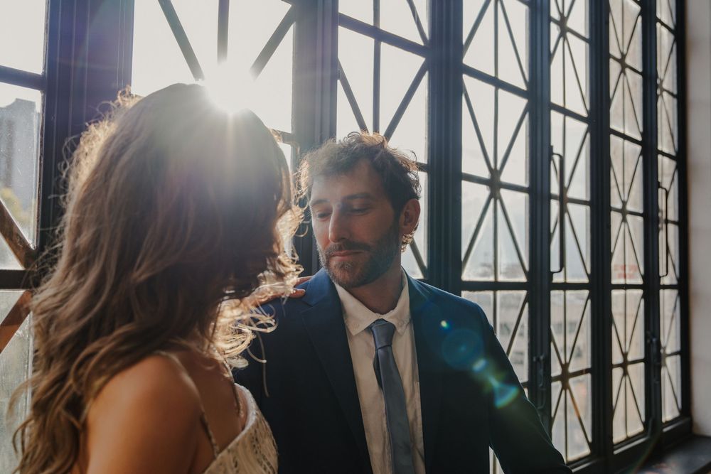 Sunlit industrial windows frame couple in intimate moment.
