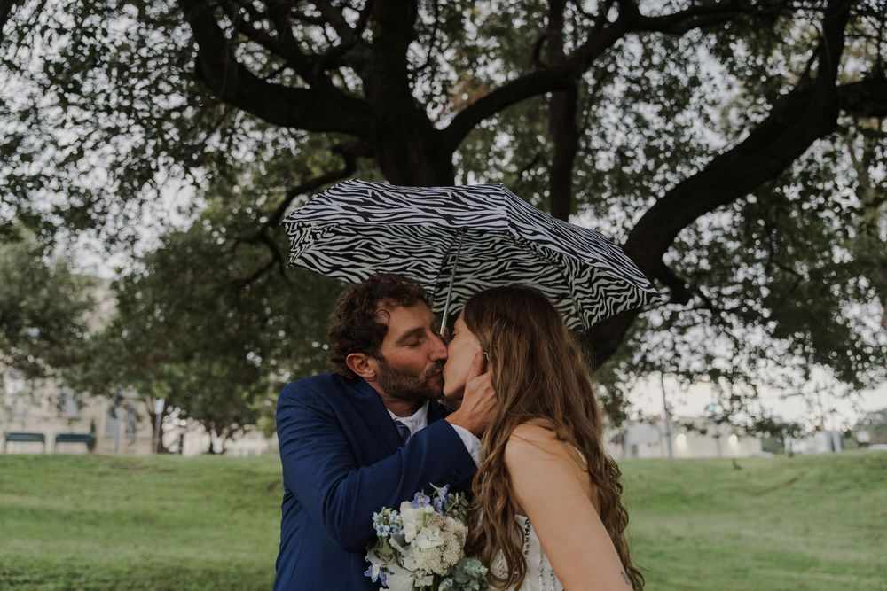 A couple shares a romantic moment under a zebra-print umbrella in a park setting.