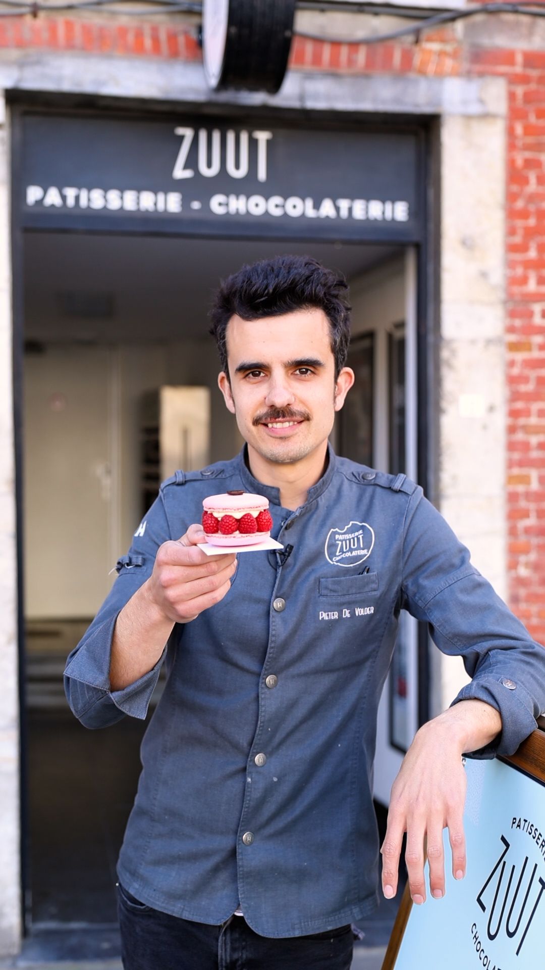 Staff member in uniform presenting dessert outside ZUUT patisserie and chocolaterie.