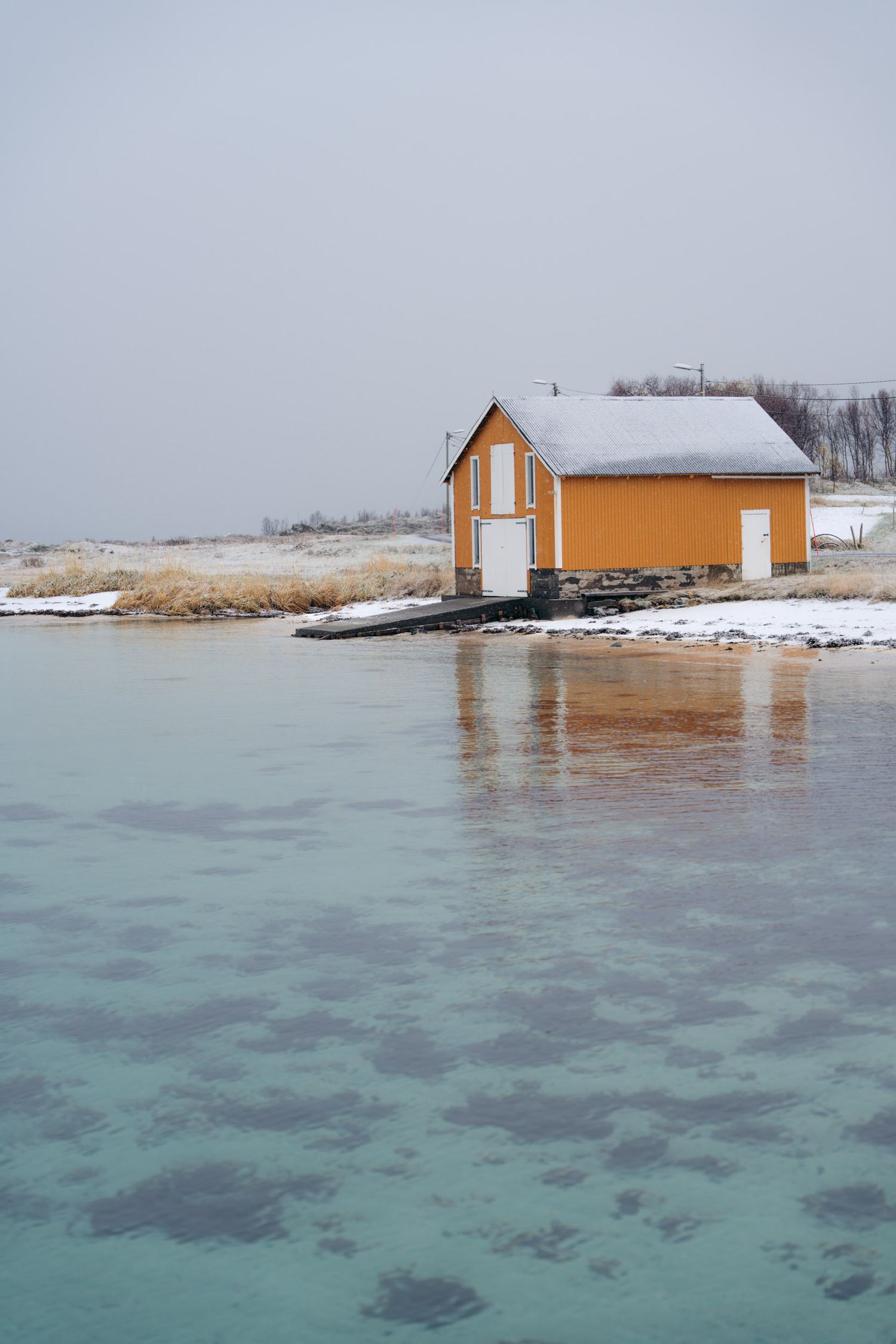 rorbu jaune au bord d'une plage à l'eau turquoise à kvaloya proche de tromso sous la neige