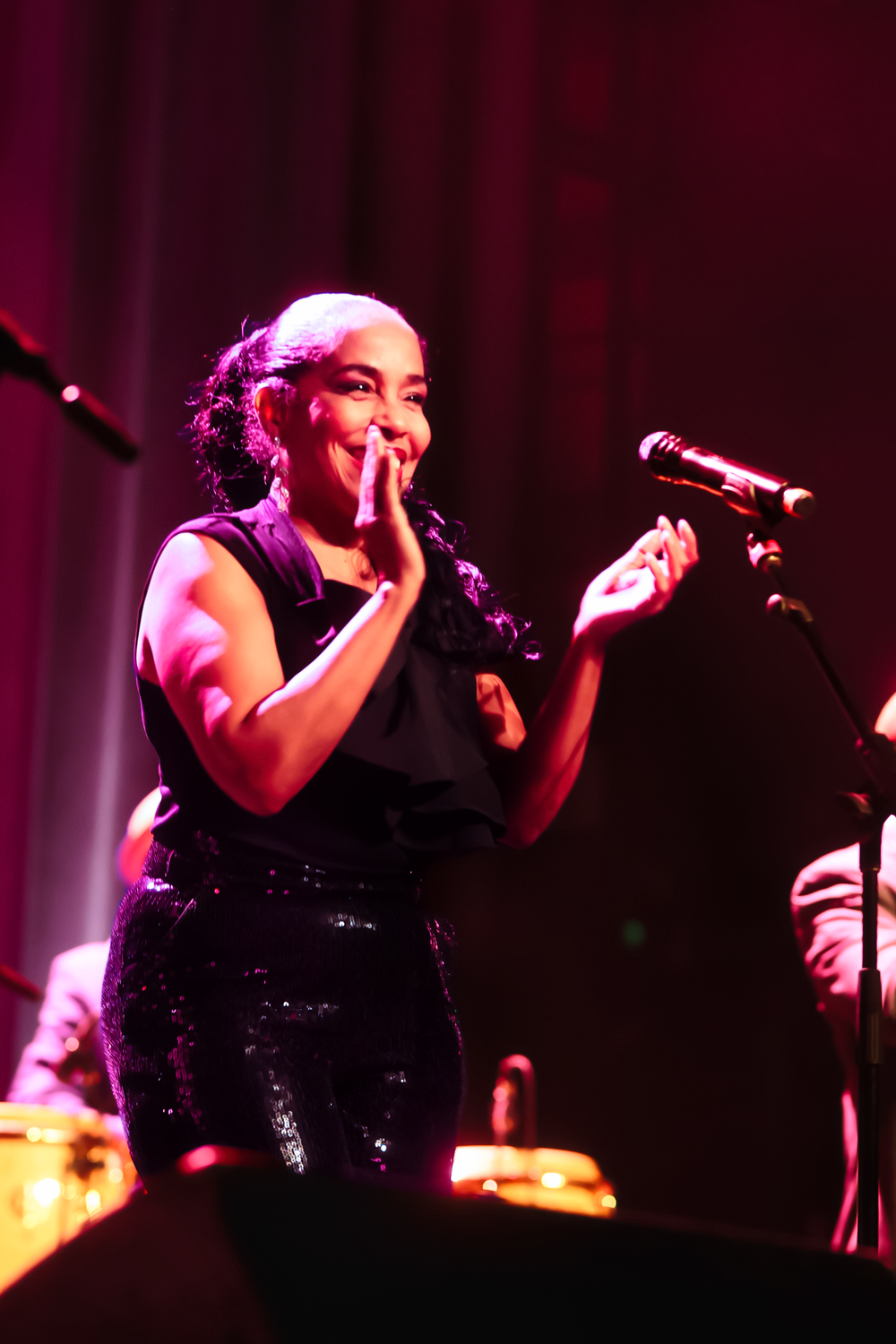 A performer in a black sequined dress sings passionately on stage under dramatic purple lighting during a concert.