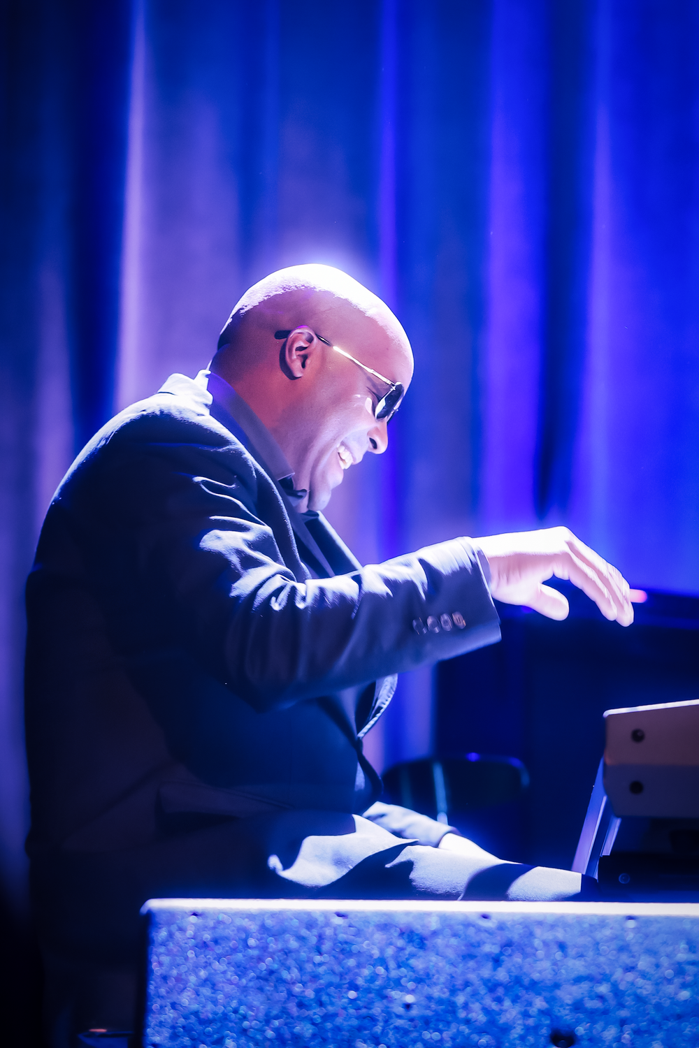 A pianist in a dark suit performs on stage with dramatic blue lighting illuminating the scene.