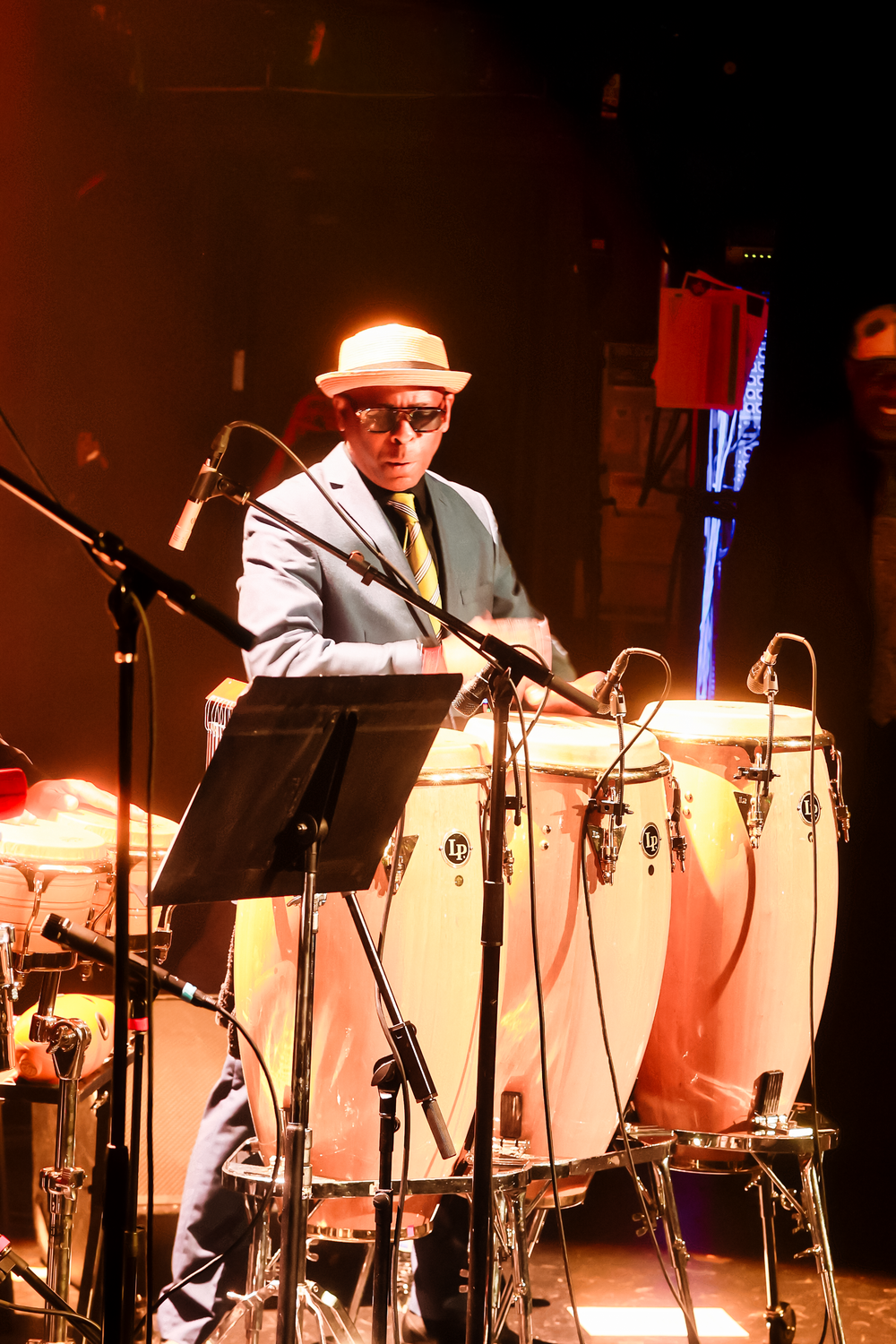 Musician performs on percussion instruments with sheet music stands and stage lighting in a dark concert venue.