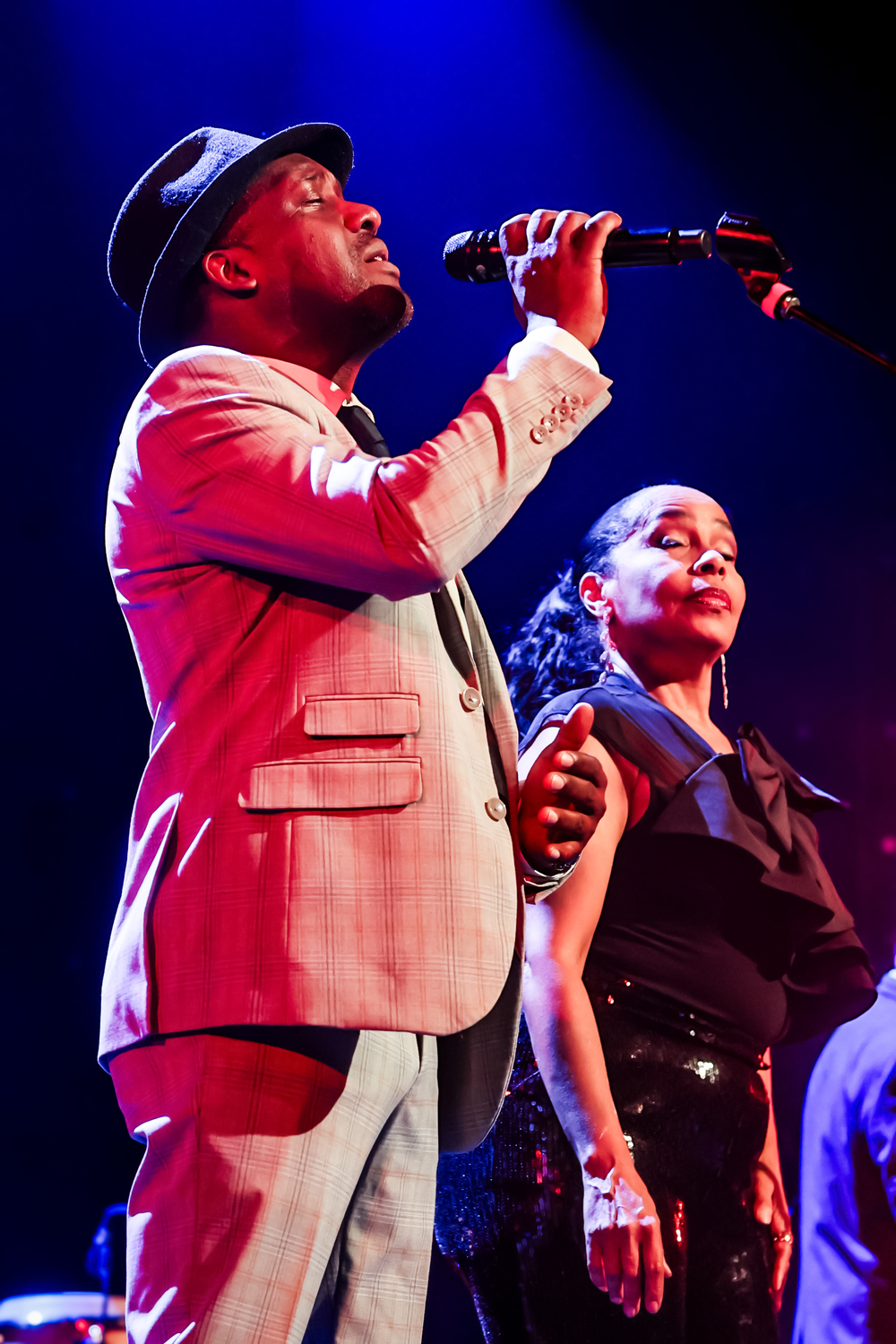 Two performers on stage singing together under dramatic blue lighting during a live concert performance.