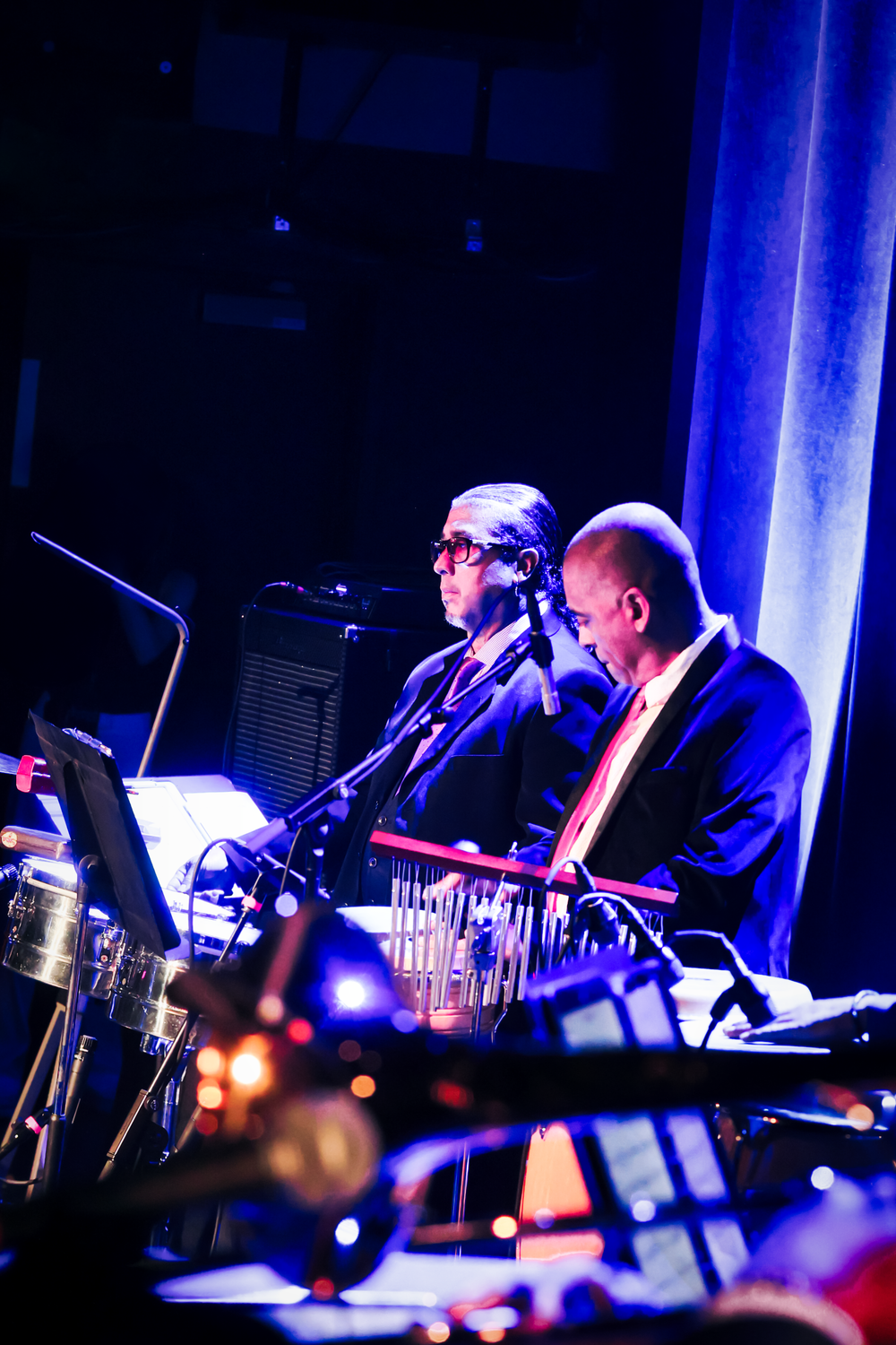 Musicians perform on stage in dramatic blue lighting during a concert performance.
