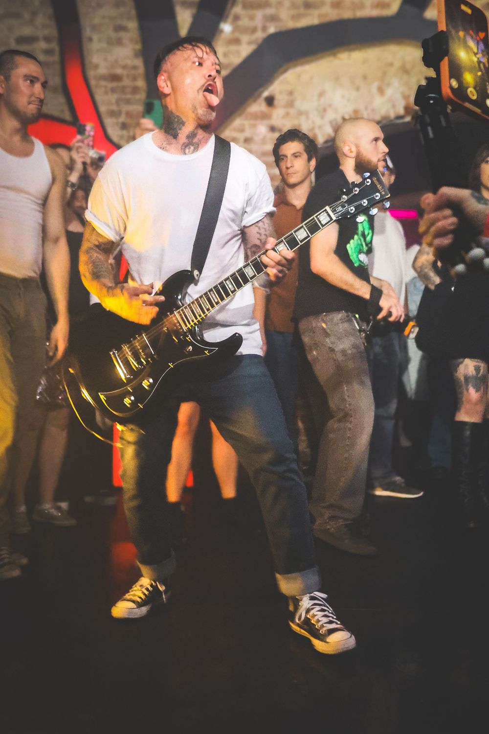 Energetic musician playing electric guitar and singing passionately at a crowded underground rock concert.