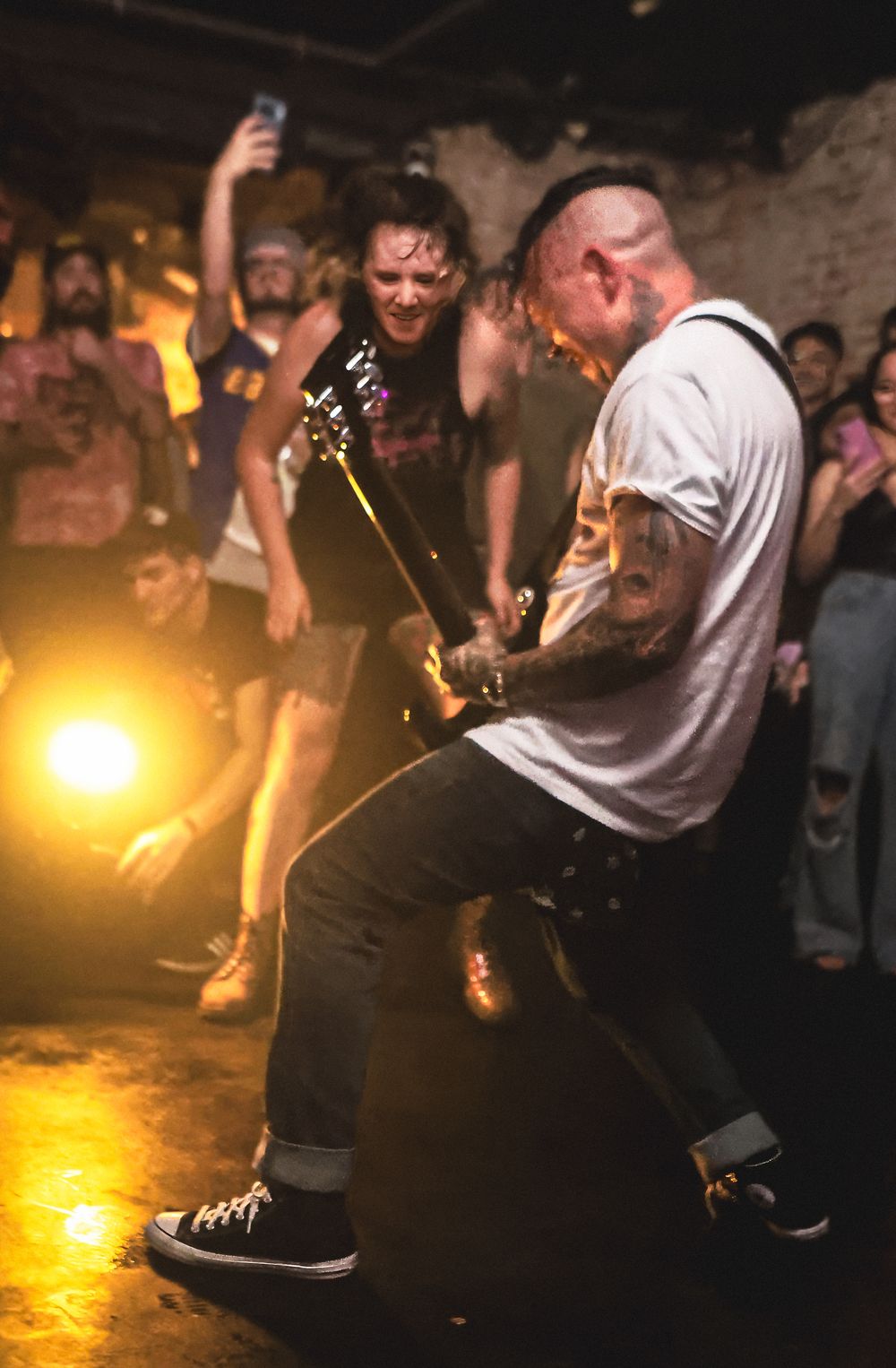 Energetic crowd dancing and moshing at a dimly lit underground rock concert with warm yellow lighting.