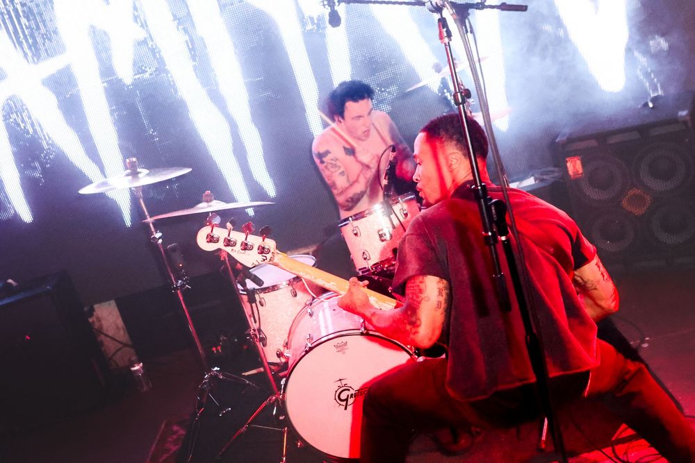 Dramatic red stage lighting illuminates a drummer performing during a live concert set.