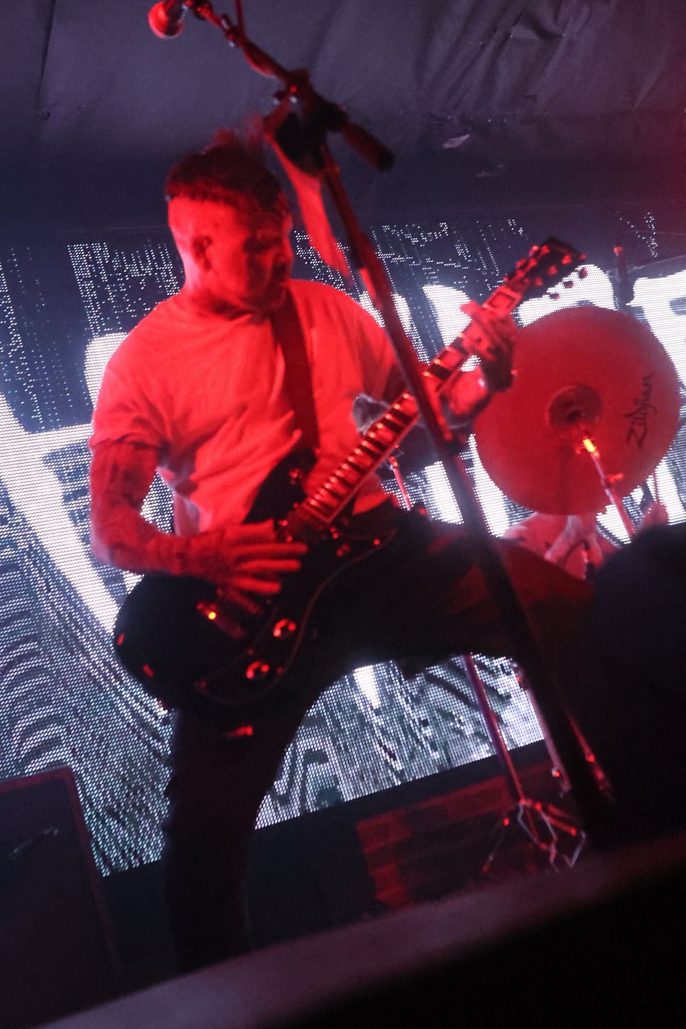 Musicians perform on stage bathed in dramatic red lighting against a dark background with visual projections.